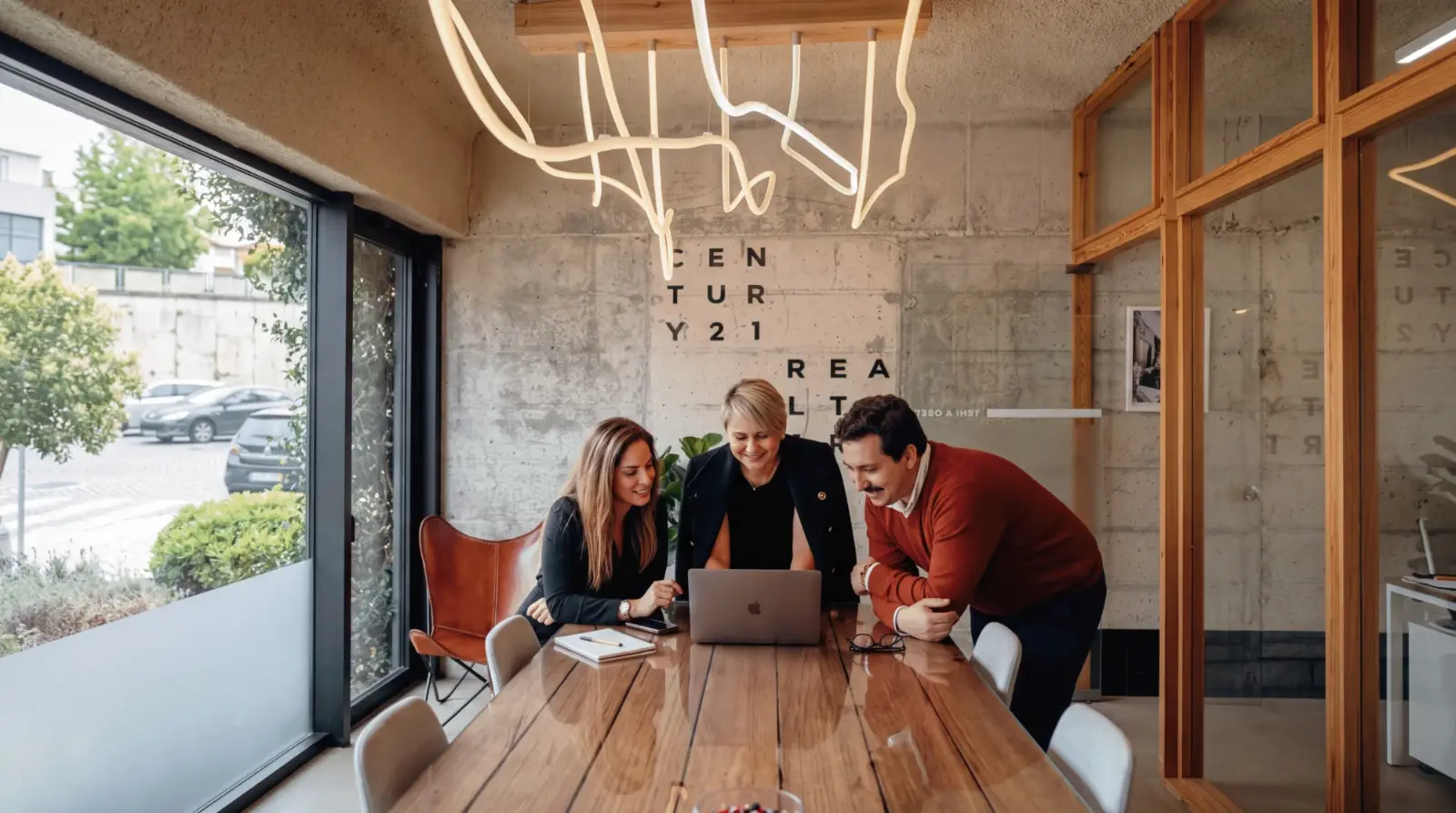 Três consultores da Century 21 Realty Art a olhar juntos para o mesmo portátil